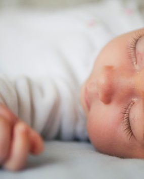 Un bébé endormi sur le dos, détendu et serein, dans une ambiance douce et rassurante.